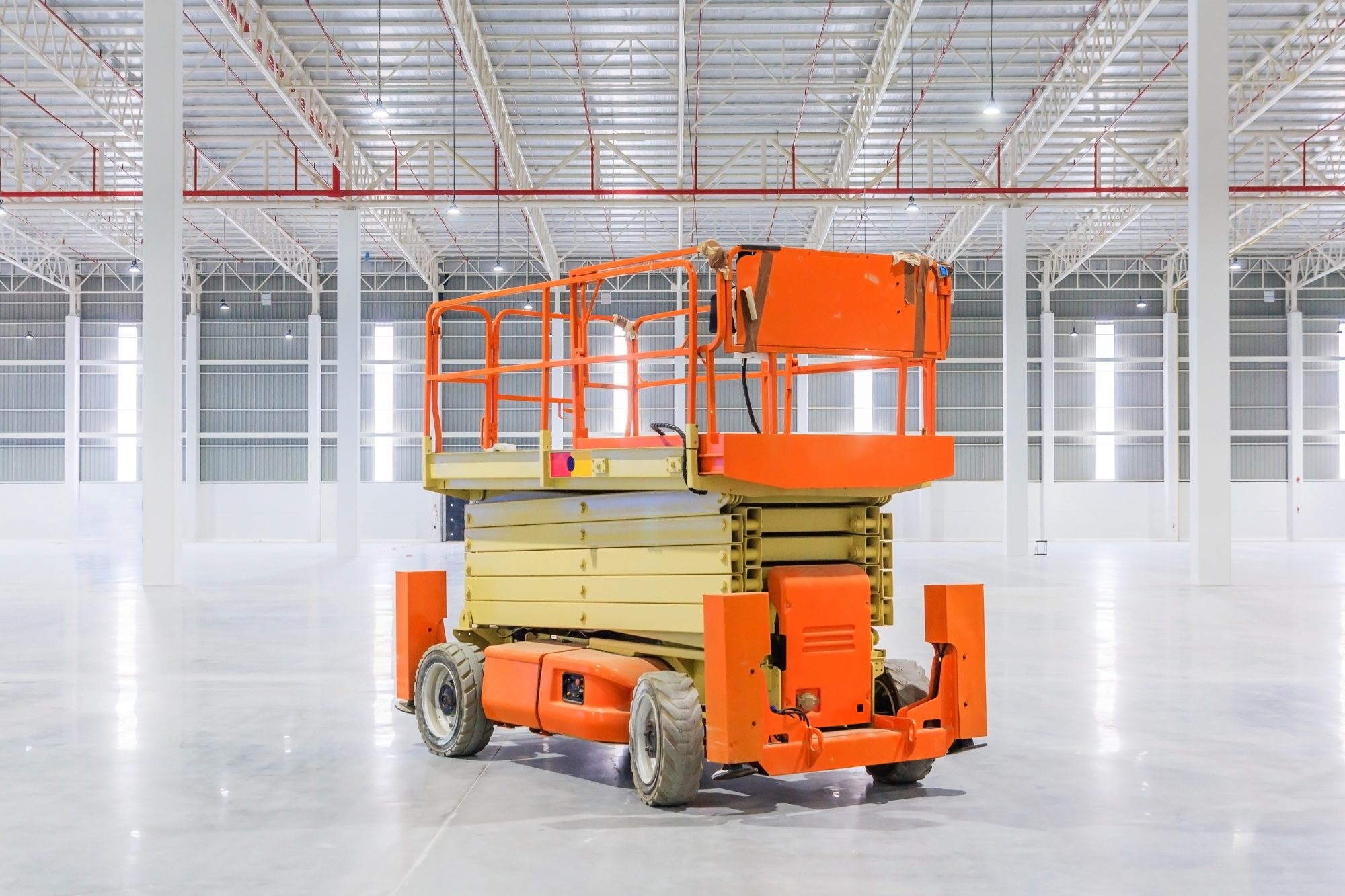An orange scissor lift with its platform lowered, in an empty warehouse